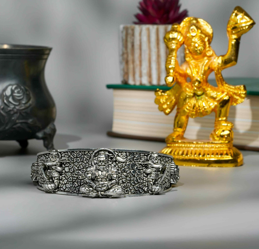 Silver bracelet with intricate designs next to a gold statue on a neutral background