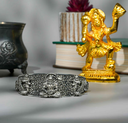 Silver bracelet with intricate designs next to a gold statue on a neutral background