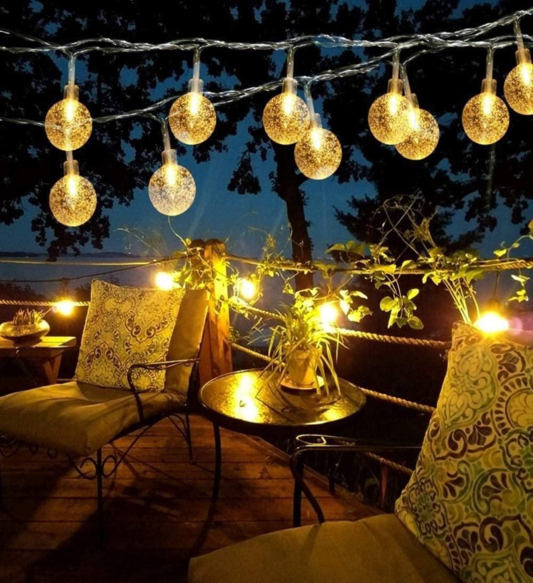 String lights with decorative bulbs hanging above a patio area with chairs and a table.