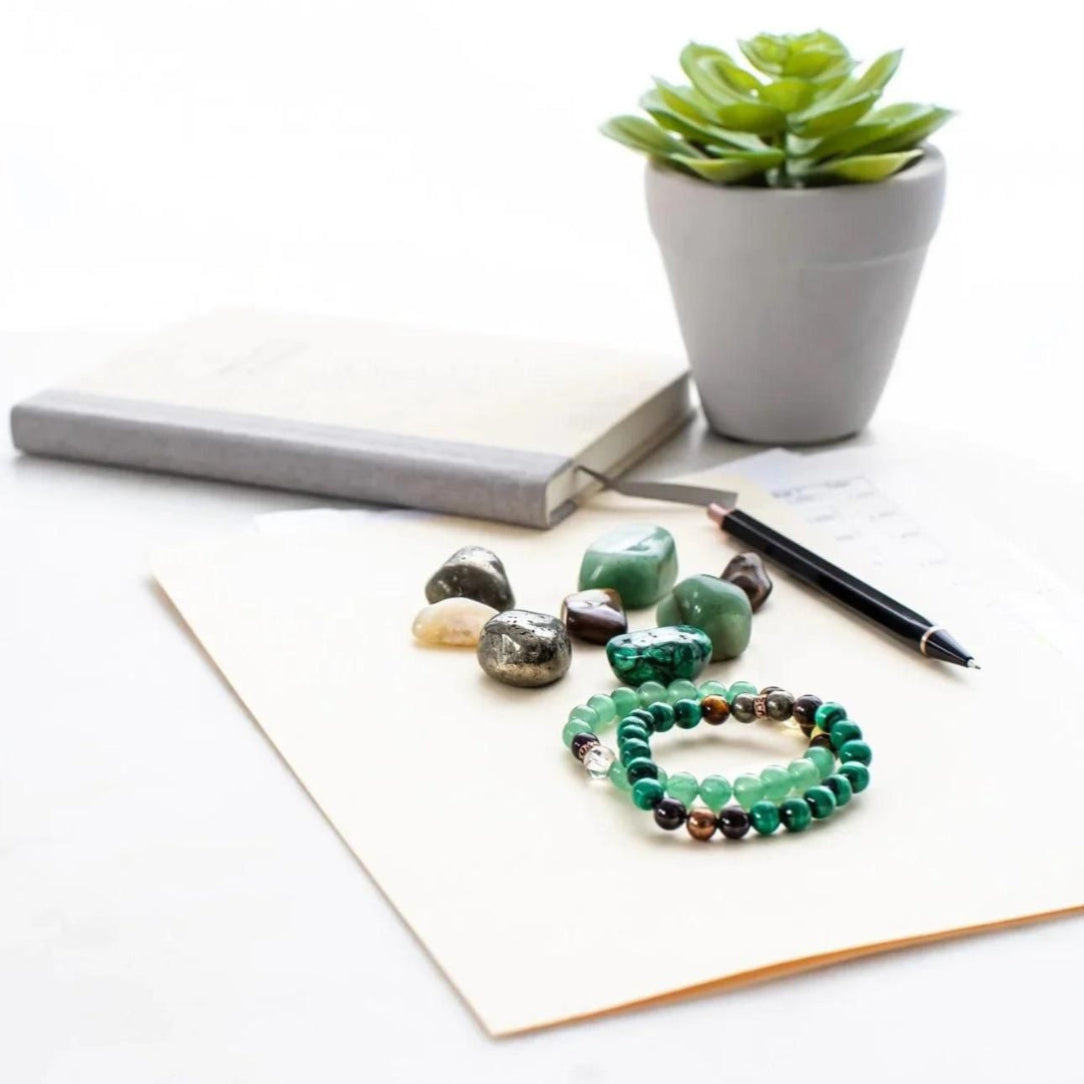 Set of beaded bracelets on a white surface with a plant and pen in the background