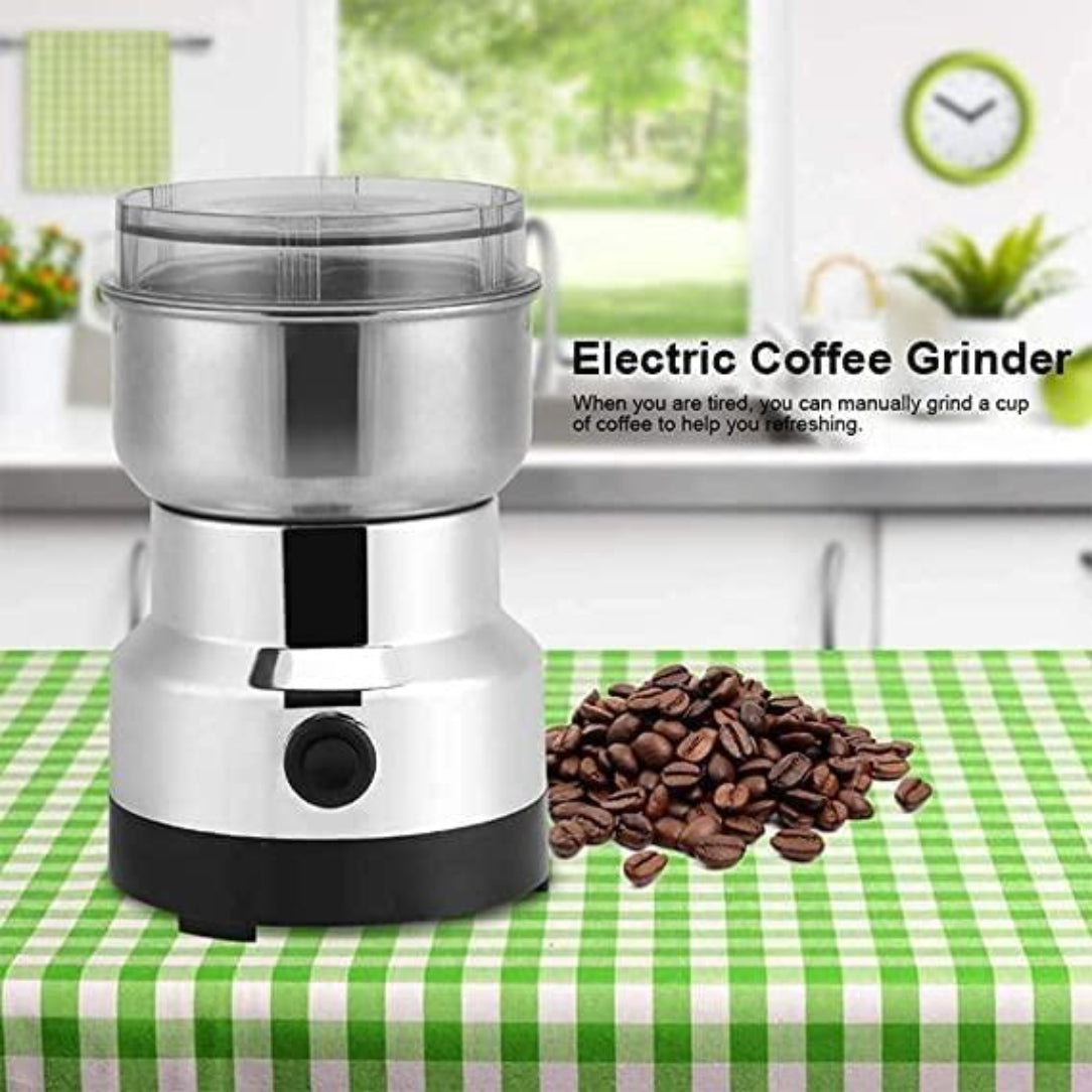 Electric coffee grinder on a green checkered tablecloth with coffee beans next to it, kitchen setting in the background.