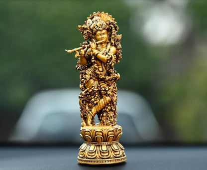 A gold-colored idol of Lord Krishna placed on a car dashboard.