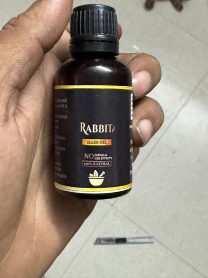 Hand holding a bottle of Rabbit hair oil with a black cap and label.