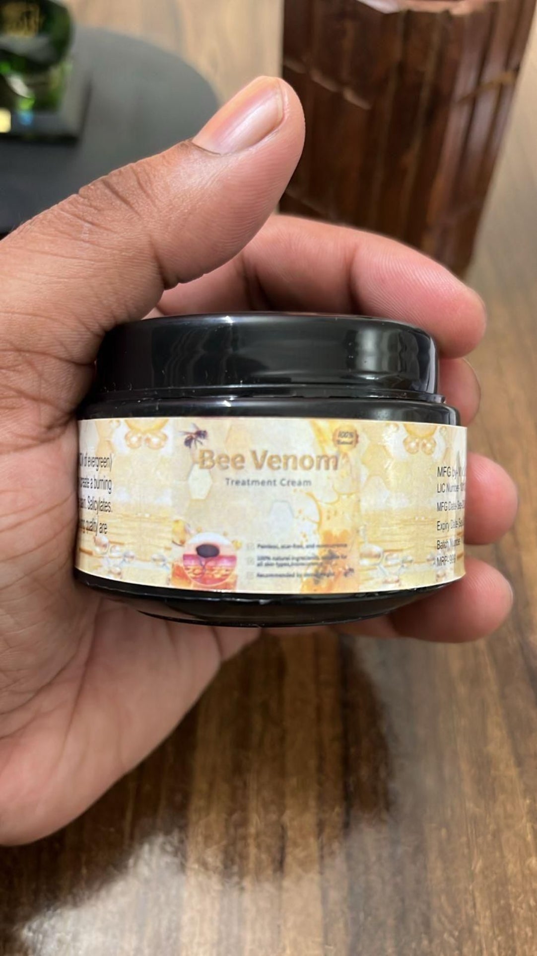 Hand holding a jar of 'Bee Venom' cream with a blurred background