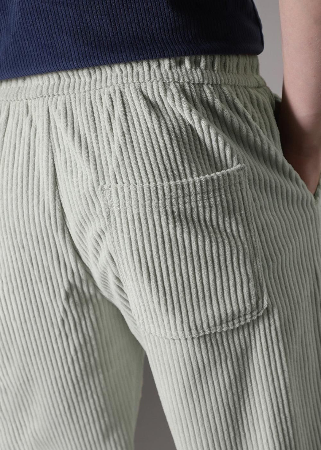 Light green corduroy pants with a pocket detail on a neutral background
