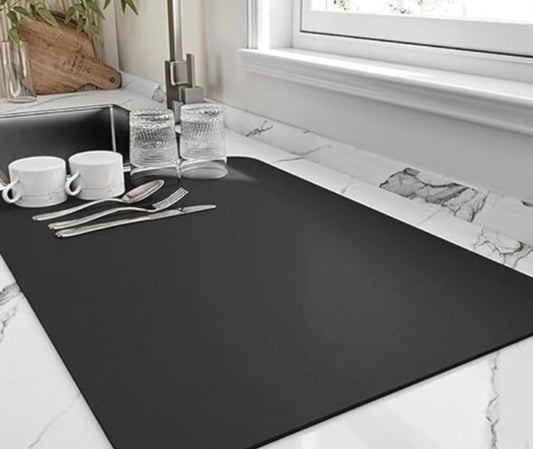 Black mat on a kitchen counter with cups, glasses, and cutlery.