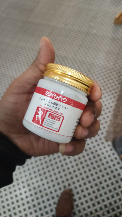 Hand holding a small white container with a gold lid against a checkered floor background