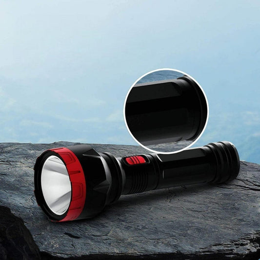 A black rechargeable LED torch with a visible LED light, placed on a rocky surface with a blurred background.