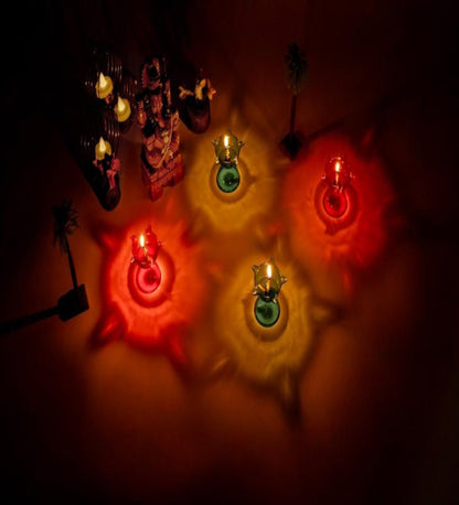 A set of five colorful 3D reflective diyas with lit wicks, placed on a surface with a warm glow.