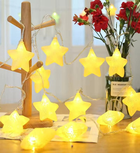 Star-shaped LED lights with a crackle effect, hanging from a wooden tree, in a warm white color, placed near a vase with flowers.