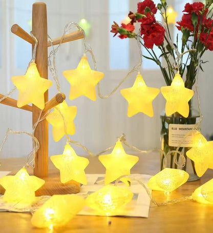 Star-shaped LED lights with a crackle effect, hanging from a wooden tree, in a warm white color, placed near a vase with flowers.