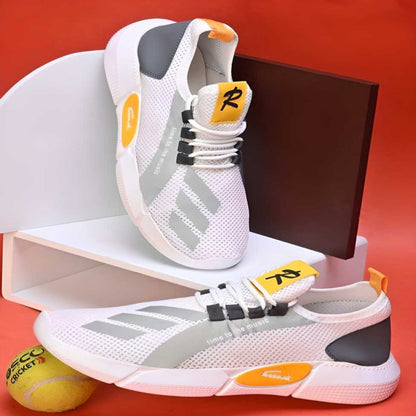 A pair of white casual shoes with yellow accents, displayed with a pair of tennis balls and a red box in the background.