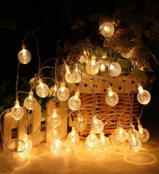A string of LED crystal balls lighting, with yellow bulbs and white cords, displayed in a garden setting.