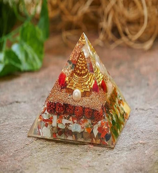 A multicolored pyramid-shaped Shri Yantra with Rudraksha beads, placed on a textured surface with a blurred green plant in the background.