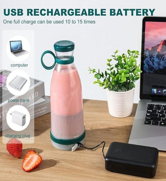 A portable mini USB rechargeable juice blender in pink color, with a green lid and base, displayed on a table alongside a laptop, a power bank, and a strawberry, indicating its compact size and portability.