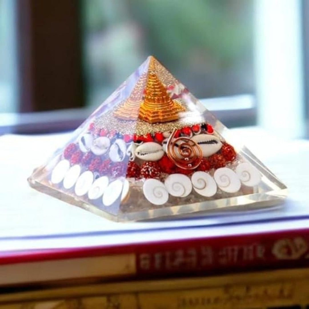 A clear crystal pyramid with a geometric design, containing a Shree Yantra and Gomati Chakra, placed on a book.