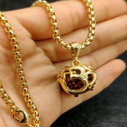 A gold-colored chain necklace with an Om symbol pendant hanging in the center, displayed on a person's hand.