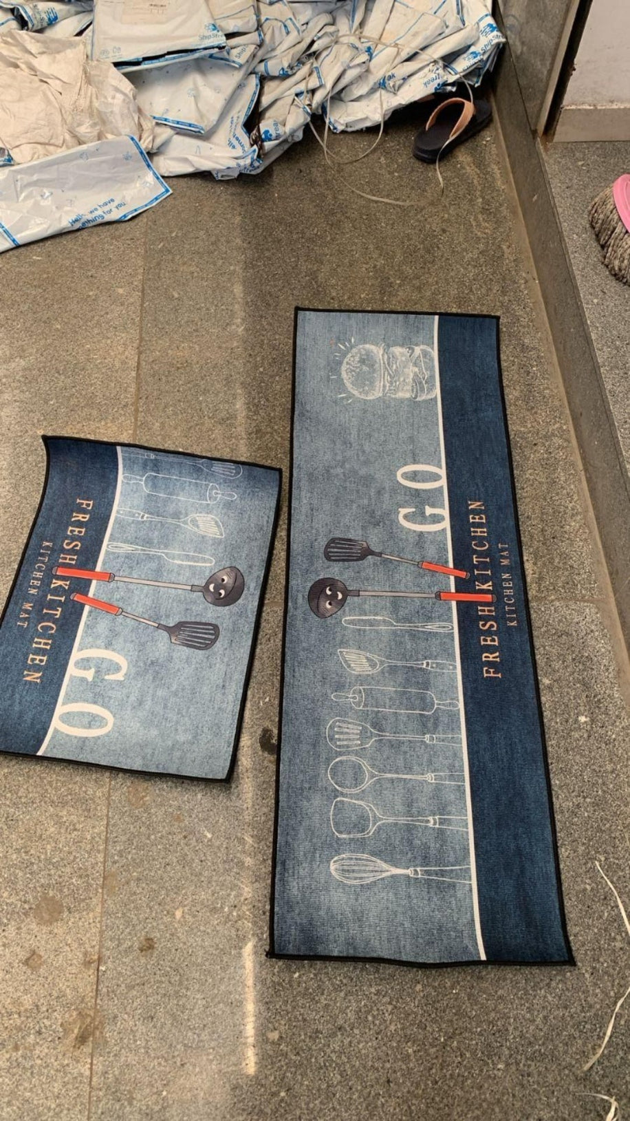 Two denim-themed kitchen mats on a floor with scattered fabric and shoes.