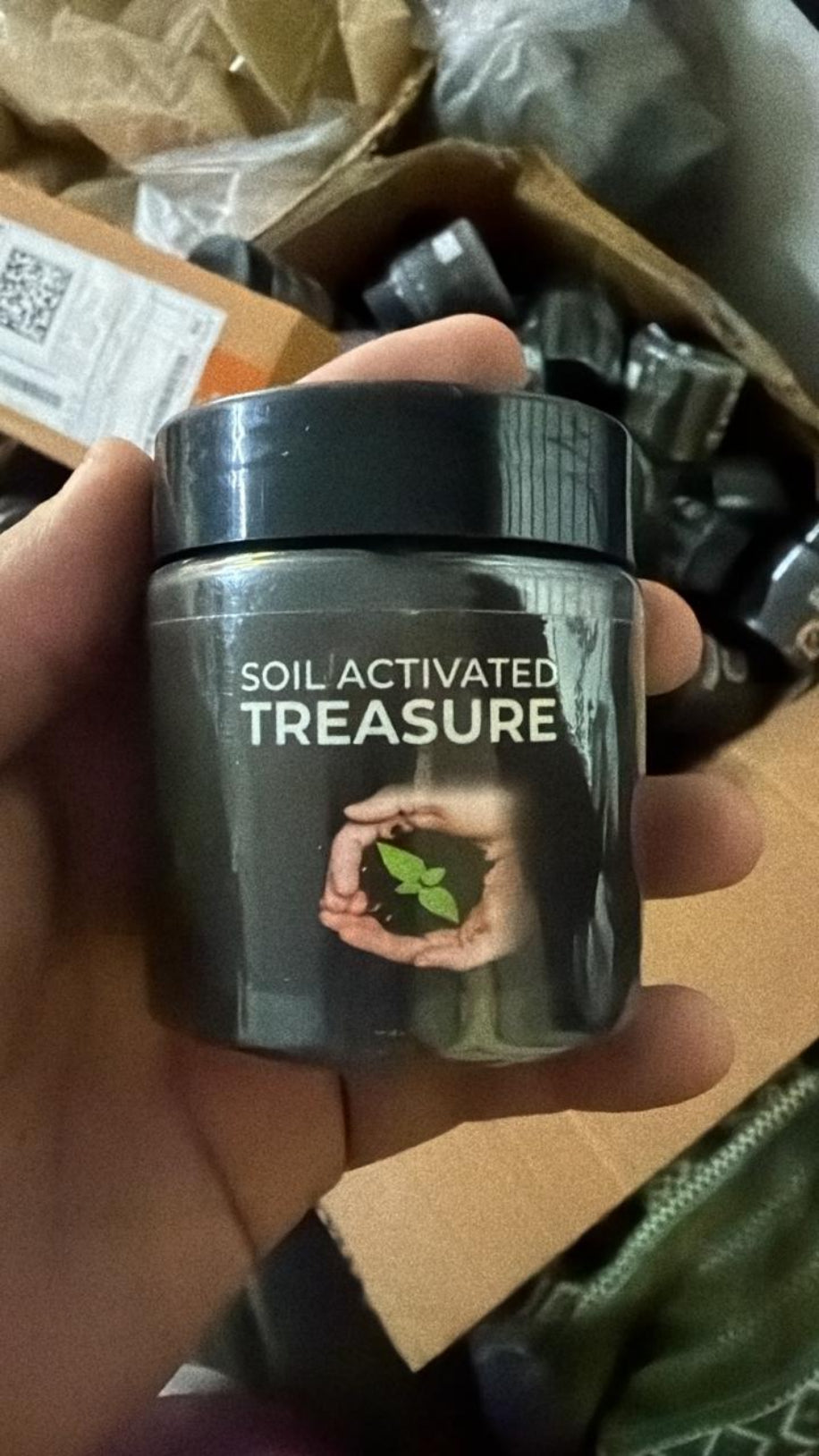 Person holding a container labeled 'Soil Activated Treasure' with a blurred background