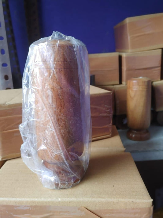 Wooden vase wrapped in plastic on a cardboard box with stacked wooden boxes in the background.