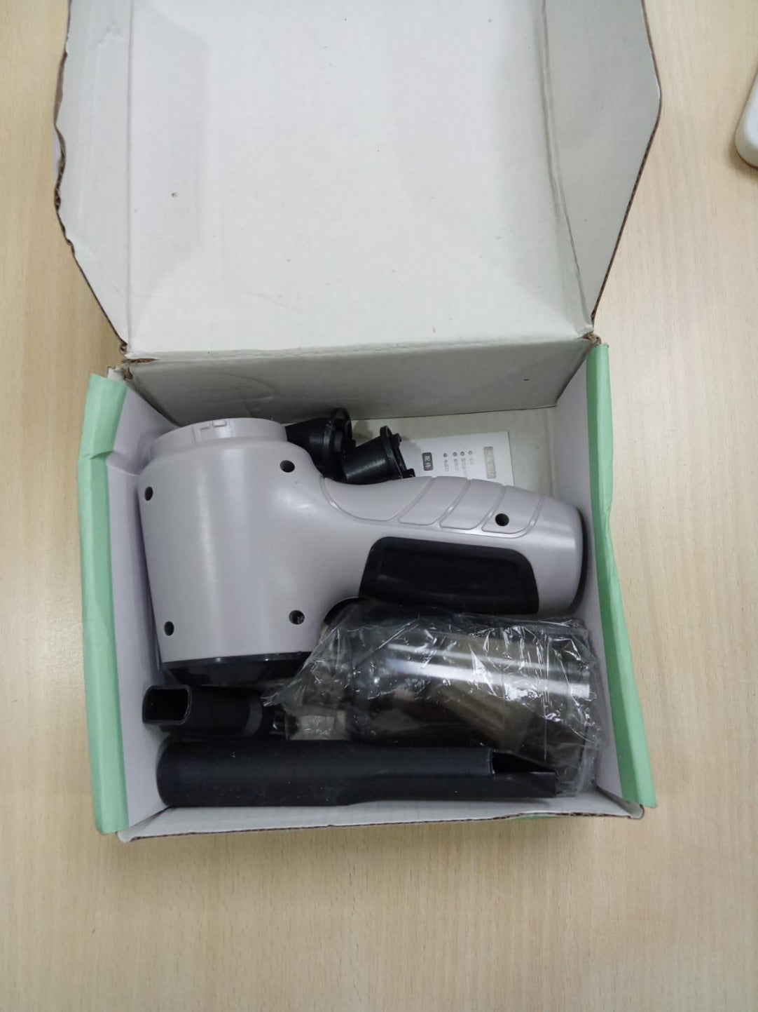 White electronic device with black components inside an open box on a beige surface.