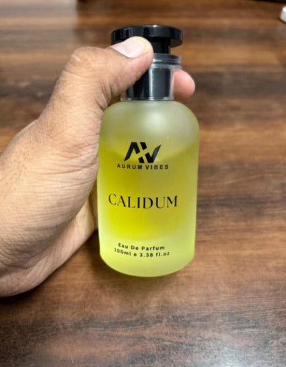 Hand holding a bottle of Aurum Vibes Calidum perfume on a wooden surface