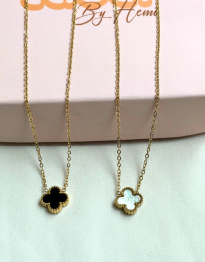 Two gold necklaces with clover pendants on a light pink background