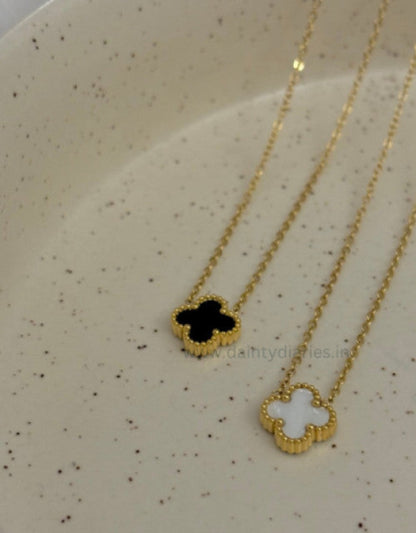 Gold necklaces with black and white clover pendants on a speckled surface