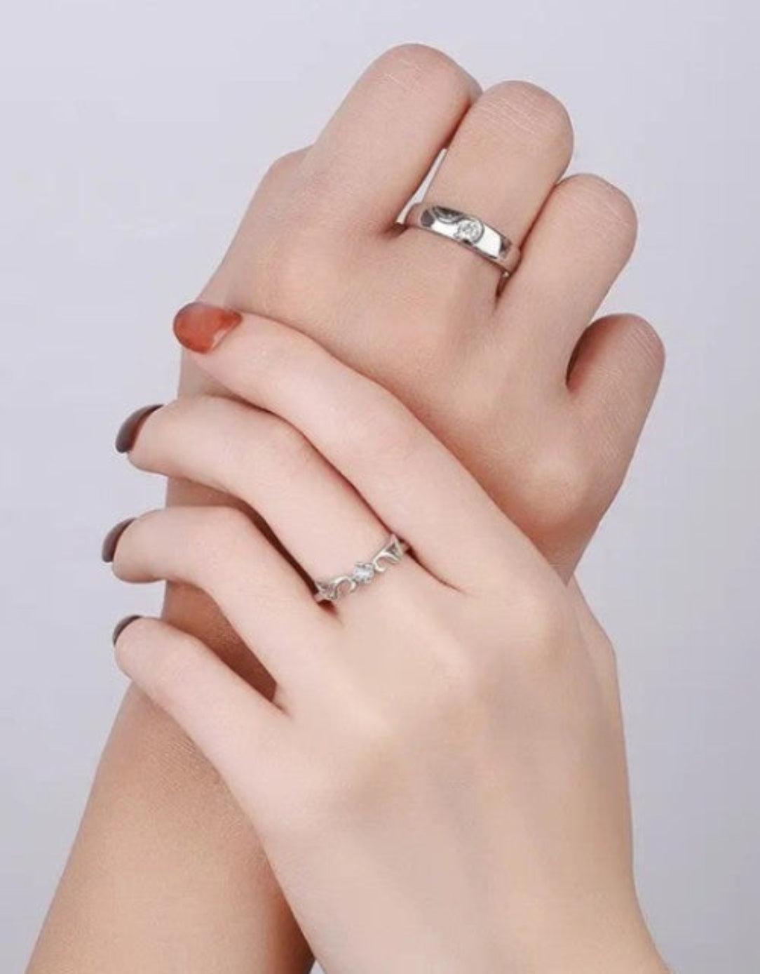 Two hands with diamond rings on a plain background