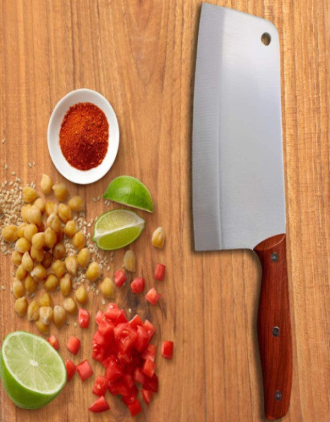 A silver-toned kitchen knife with a brown handle on a wooden surface, surrounded by chopped vegetables, limes, and a small bowl of spices.