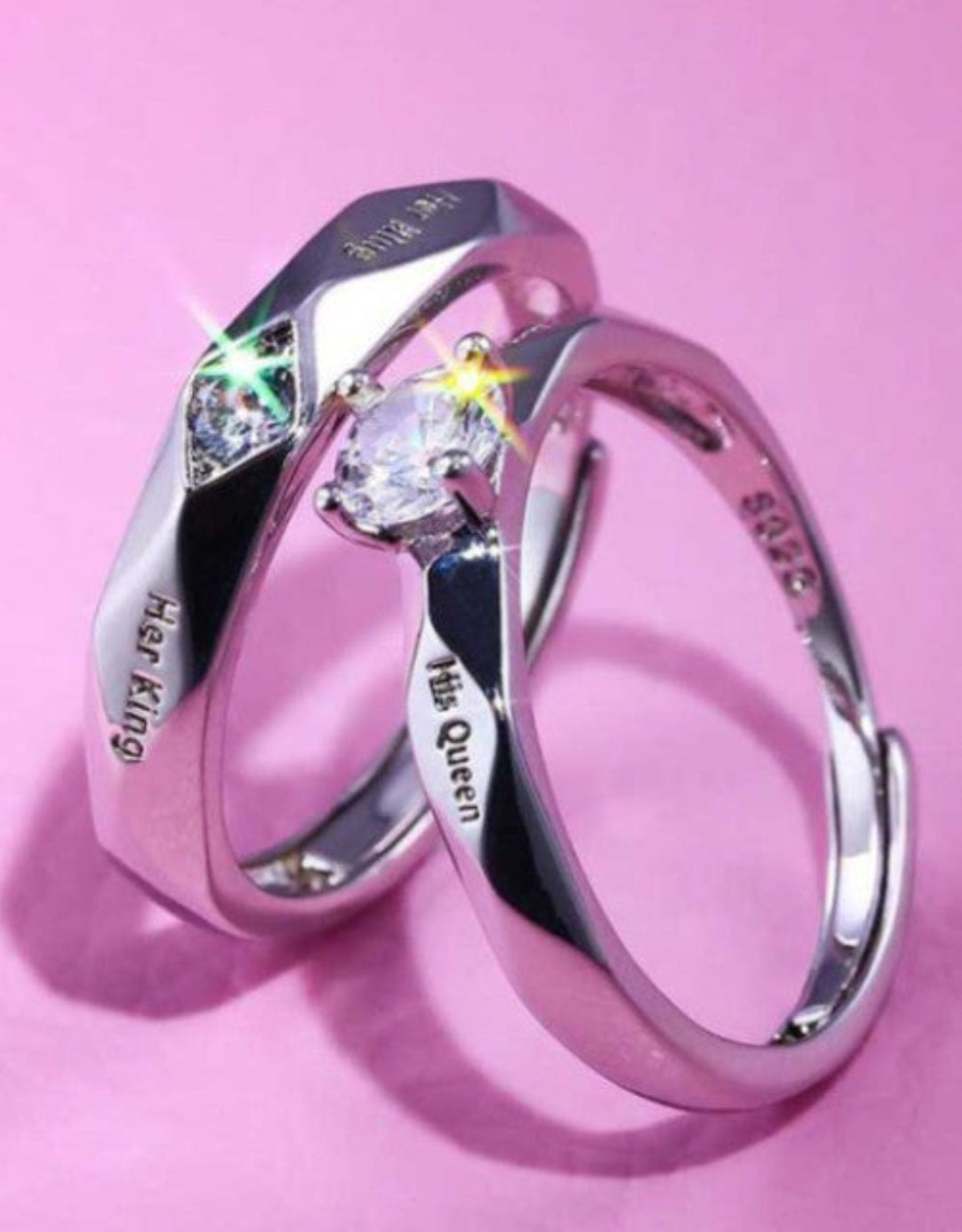 A pair of silver-colored stainless steel couple finger rings with crystal nug diamond stone accents, displayed against a pink background.